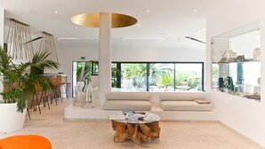 A modern lobby with a large wooden coffee table, a seating area with sofas, and a large window offering a view of greenery outside. - Hotel Cala di Greco (Bonifacio)