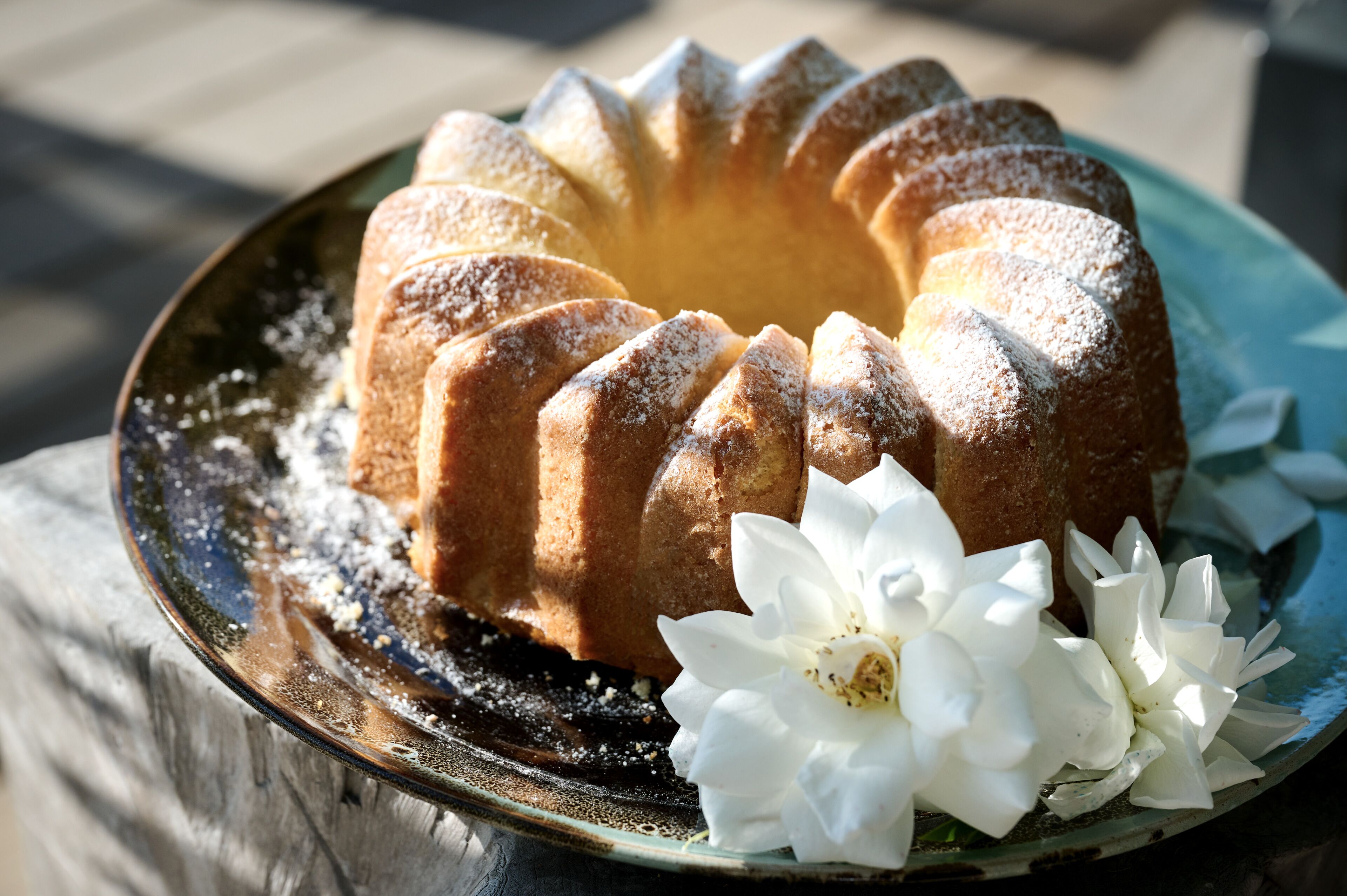 Un bizcocho Bundt en un plato de cerámica con azúcar glas y una flor blanca.