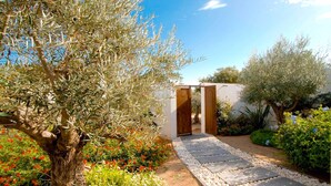 A garden pathway leading to a wooden door, surrounded by olive trees and flowering plants. - Hotel Cala di Greco (Bonifacio)