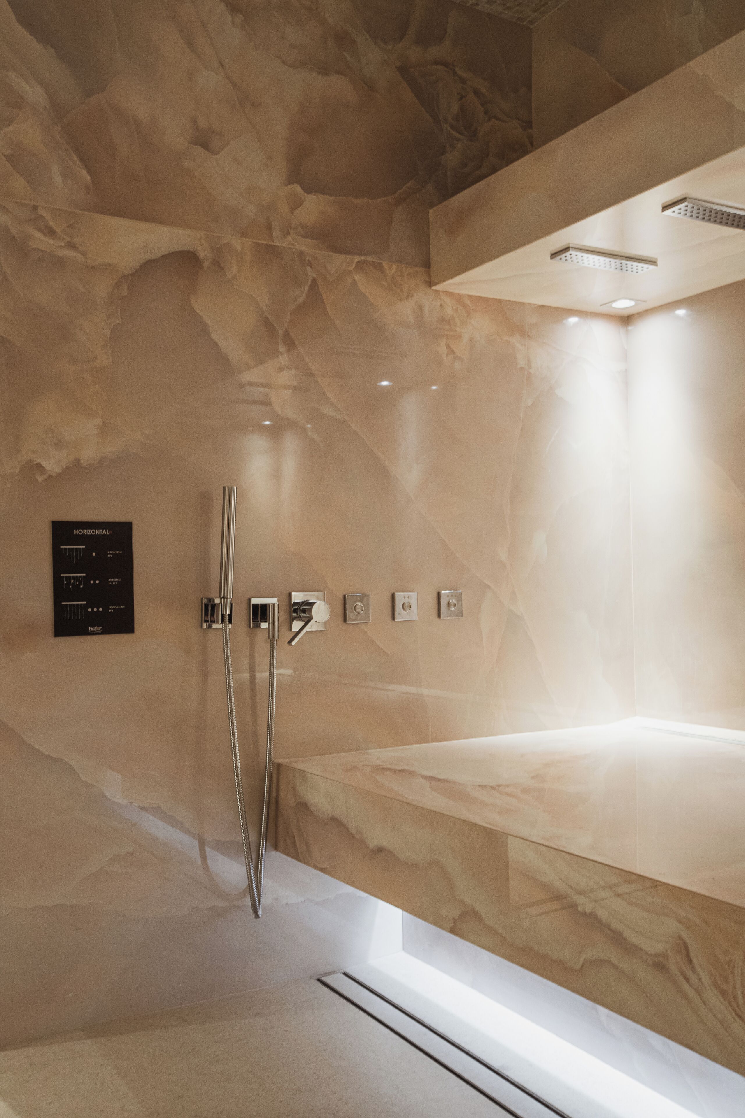 A modern bathroom with a marble wall, a built-in shower, and a control panel for water temperature and flow.