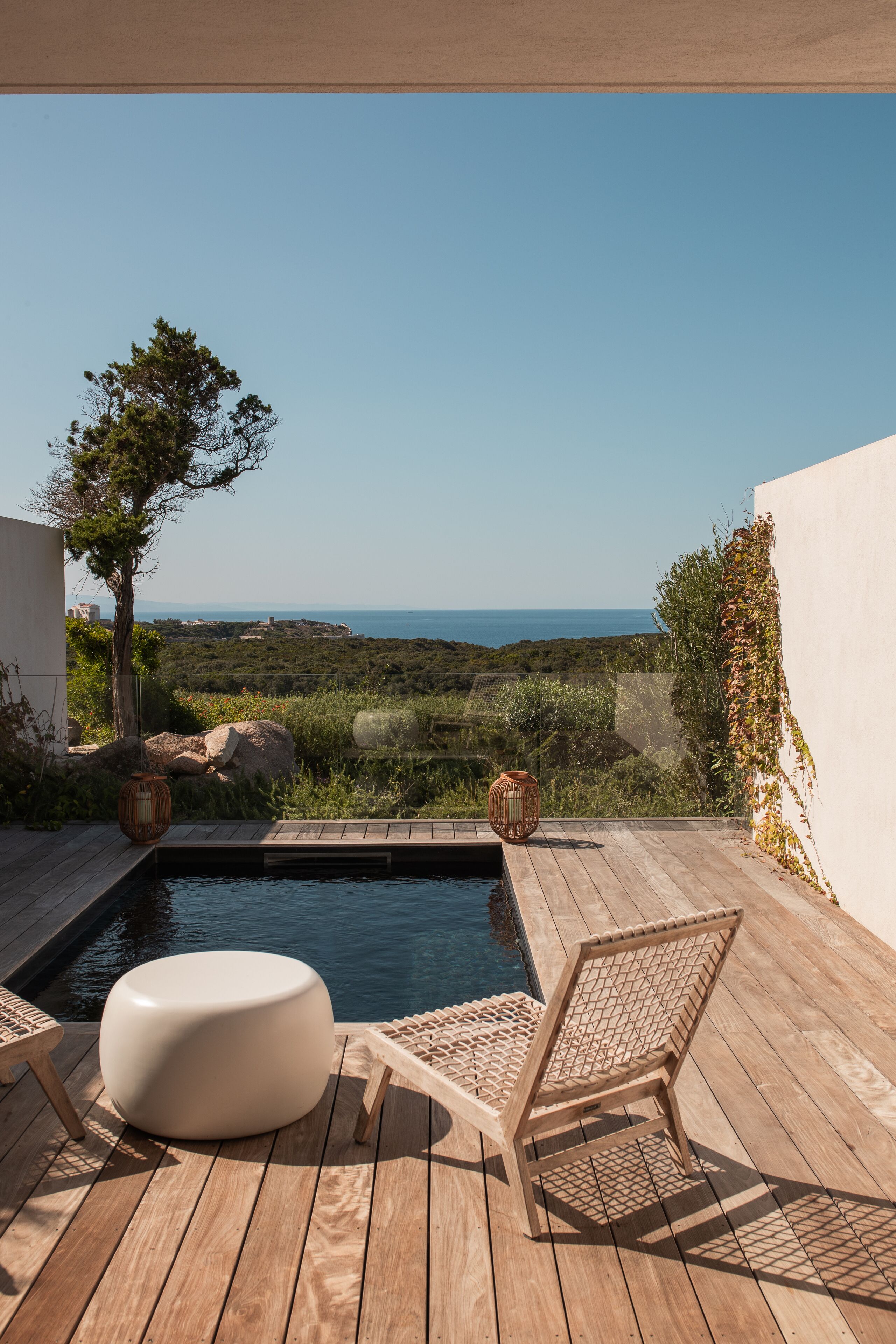 A wooden deck with a pool, lounge chairs, and a view of the sea.