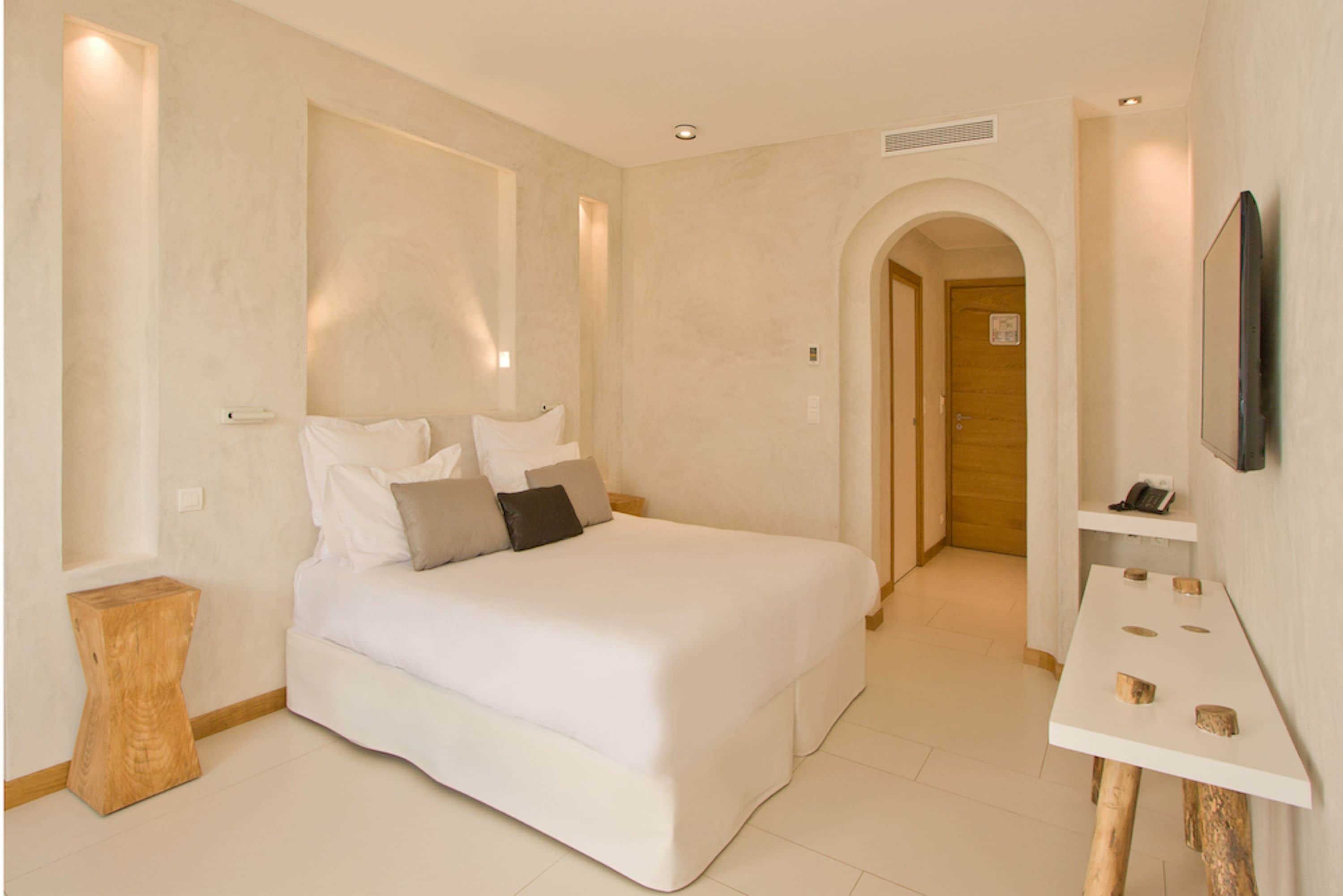 Un dormitorio moderno con una cama grande, una mesita de noche de madera y un televisor montado en la pared.