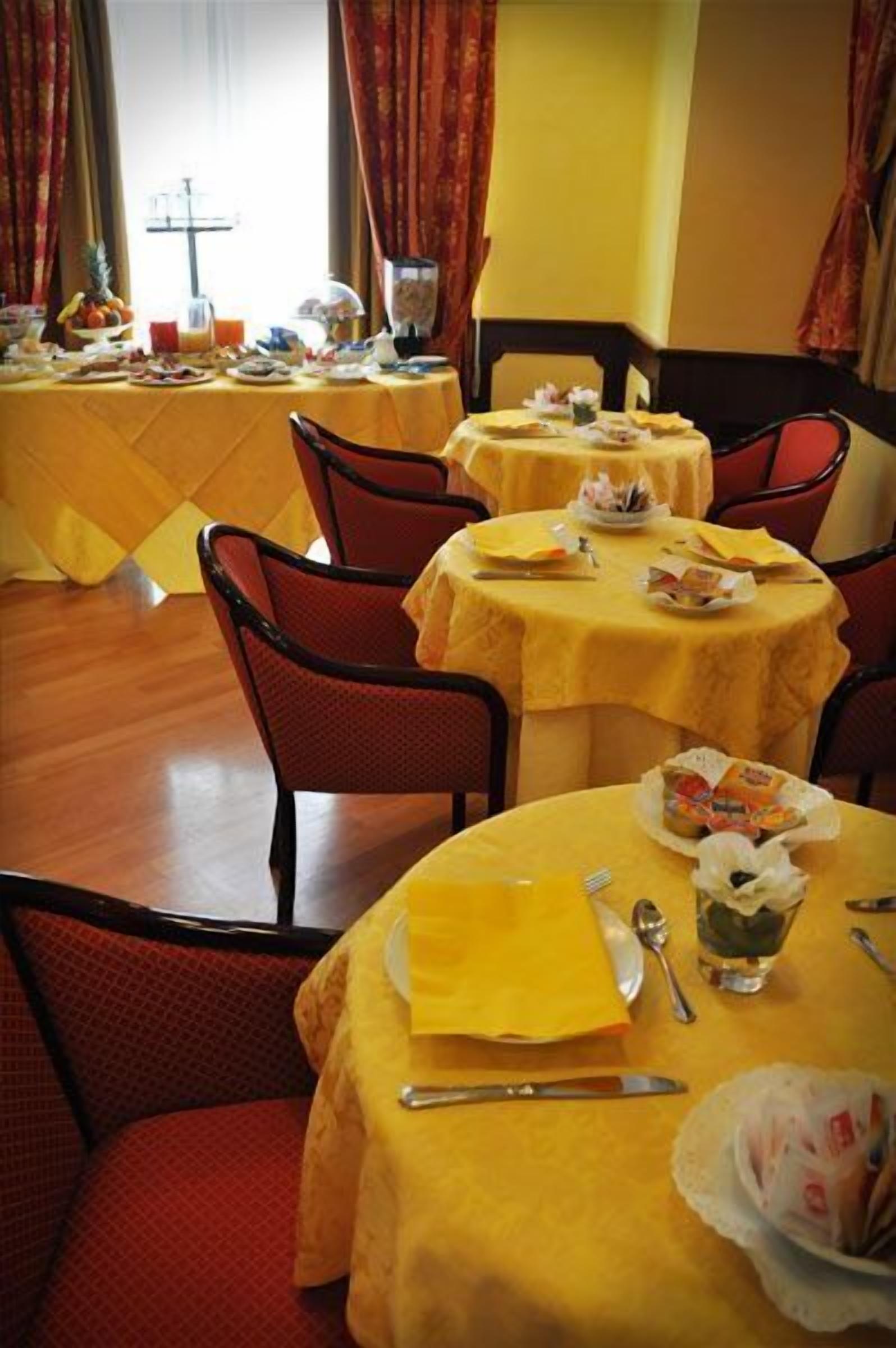 Un comedor con mesas redondas cubiertas con manteles amarillos, sillas rojas y diversos productos para el desayuno.