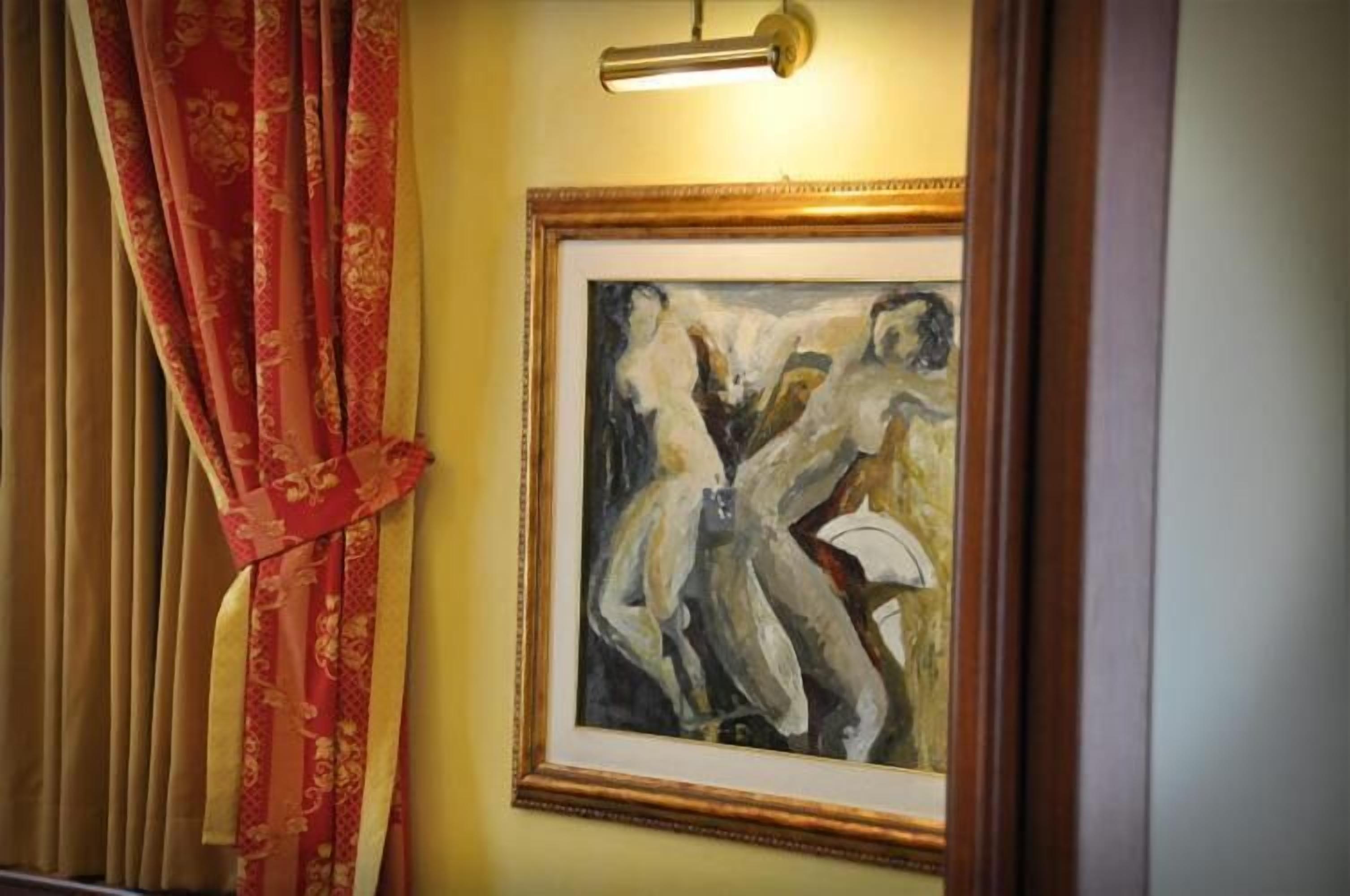Un tableau abstrait encadré accroché au mur, un rideau rouge et un luminaire.