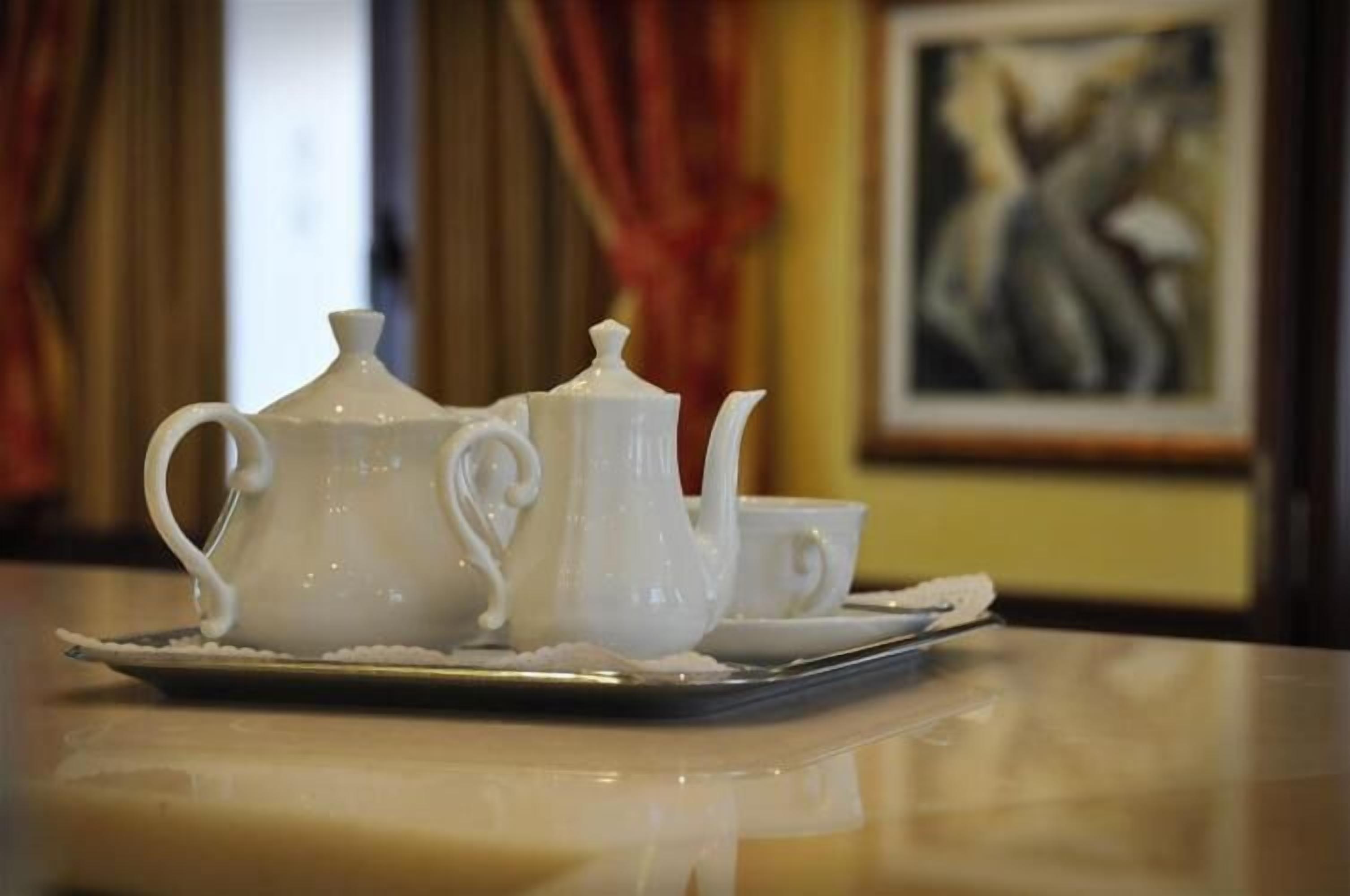 A white tea set on a tray with a painting in the background.