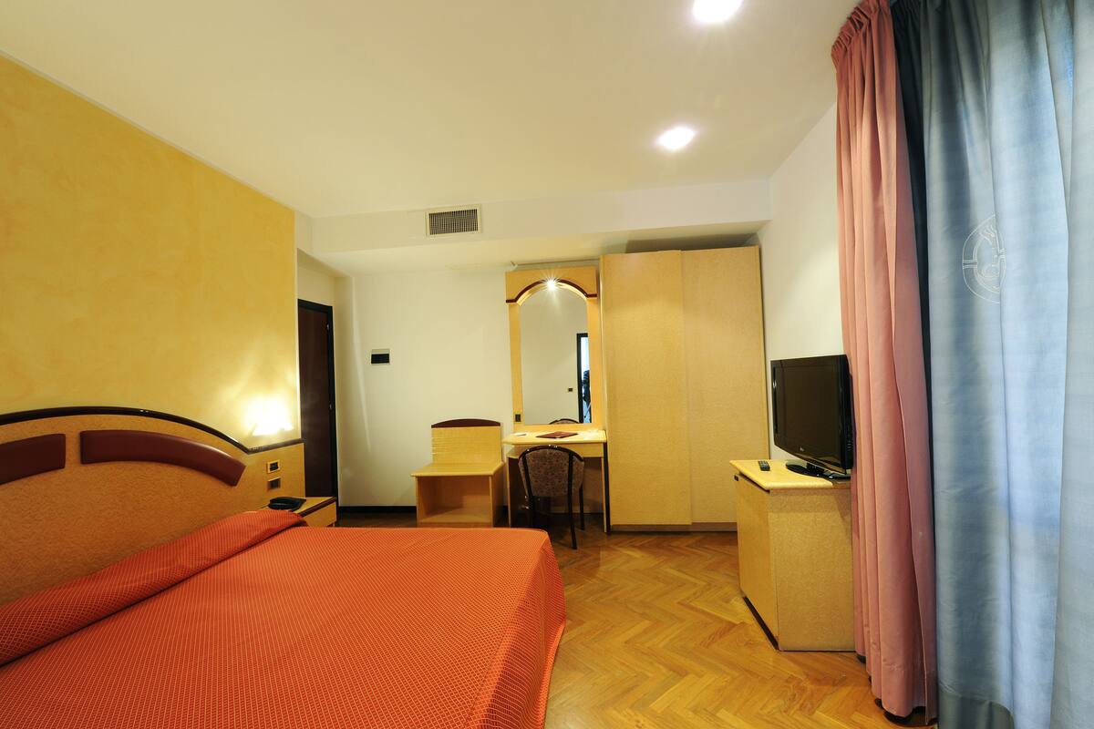 Habitación de hotel con cama, escritorio, silla, televisor y armario.
