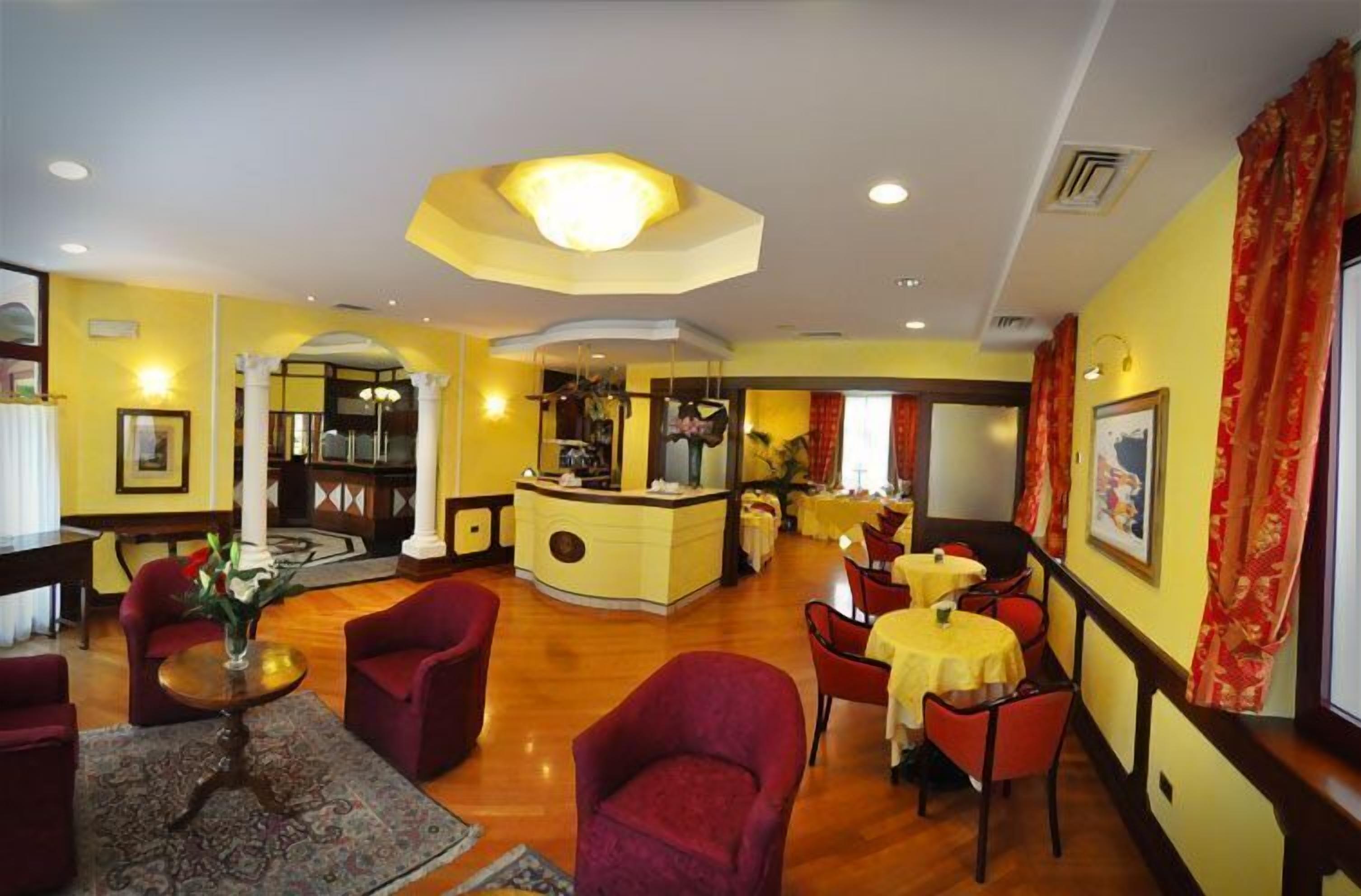 A hotel lobby with red armchairs, a central bar area, and yellow walls.