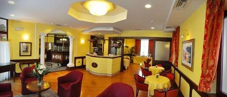 A hotel lobby with red armchairs, a central bar area, and yellow walls.