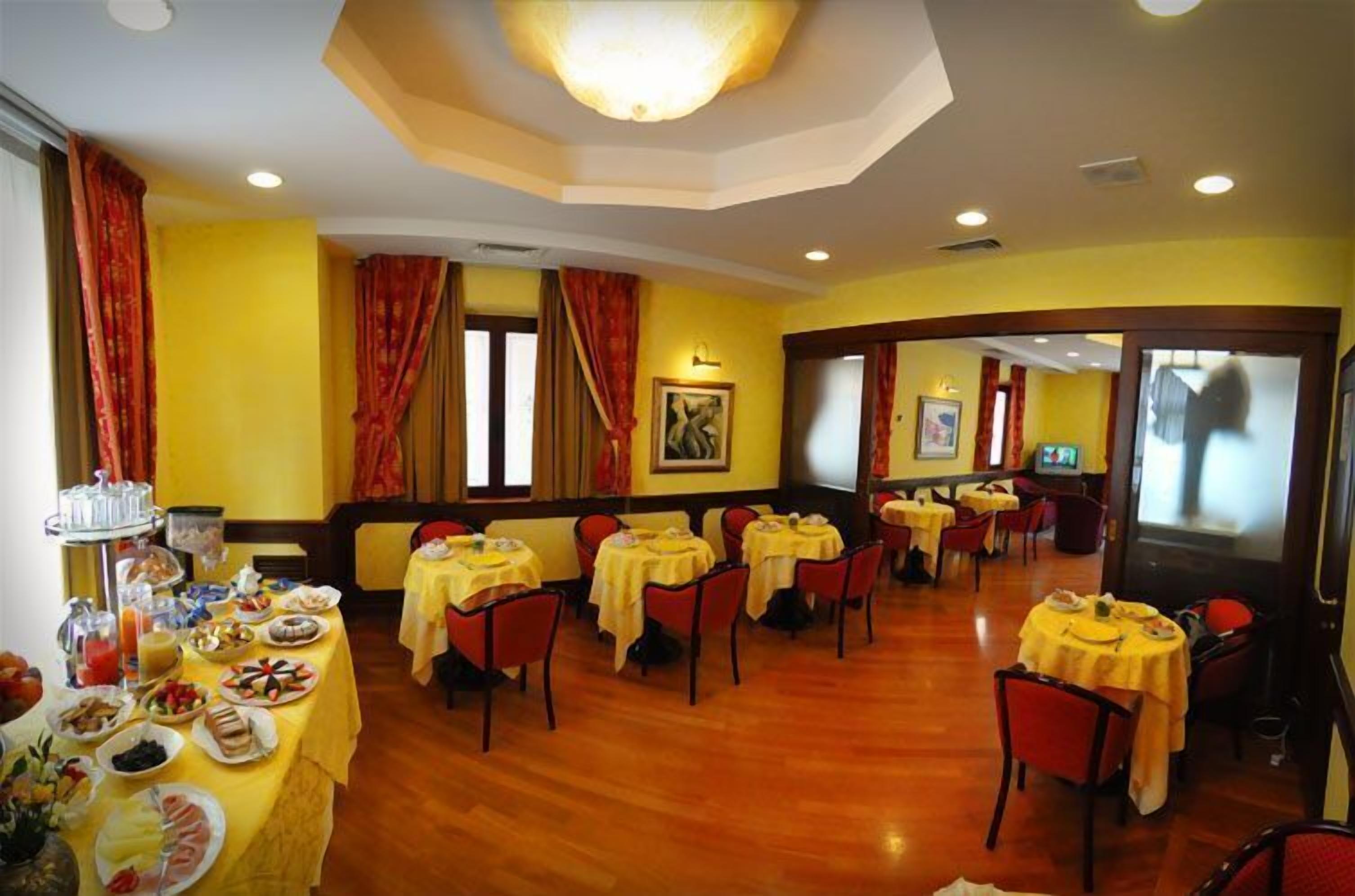 A dining area with multiple tables and chairs, a buffet with various food items, and a television screen.