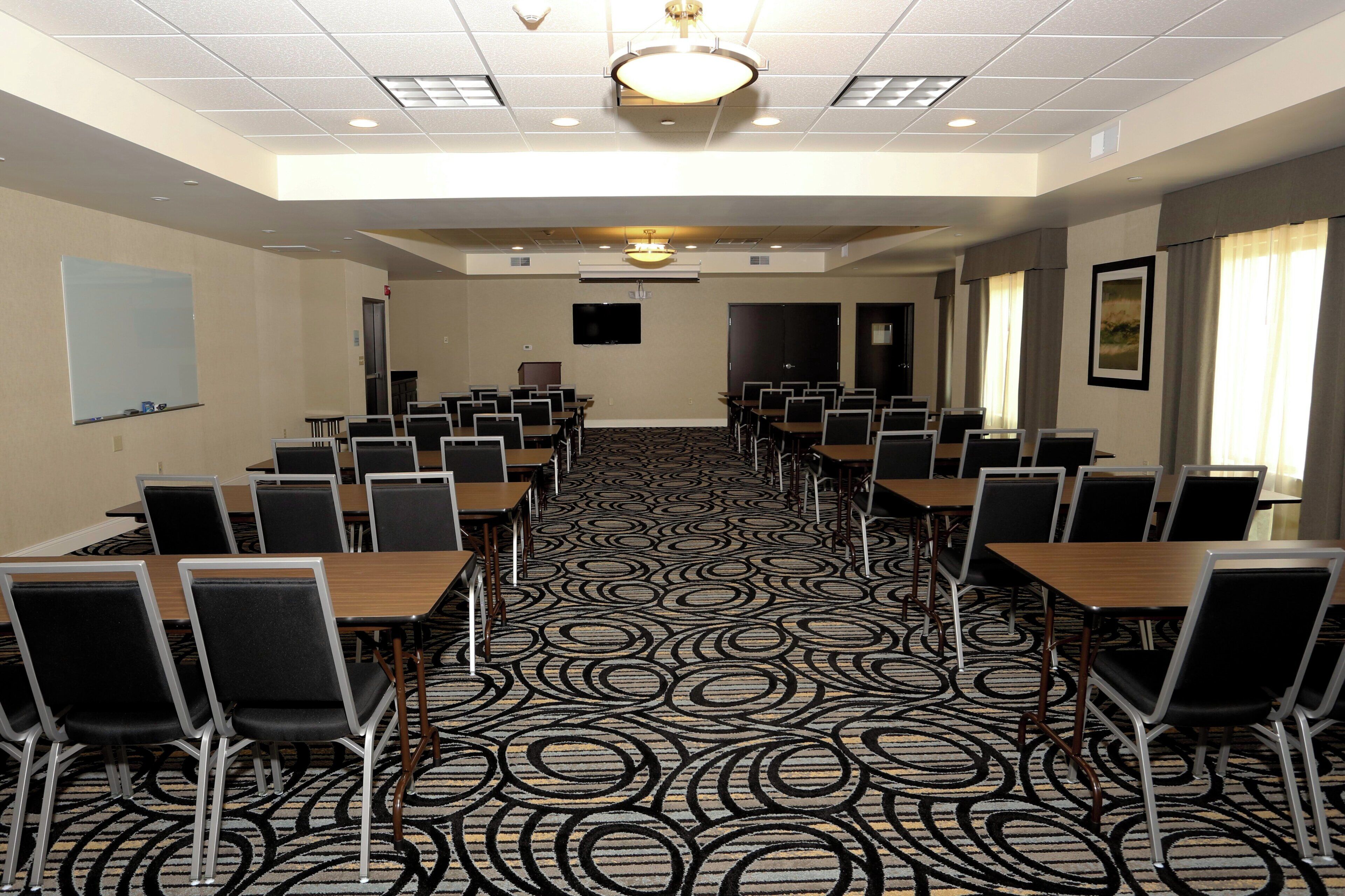 Un salón de conferencias con alfombra estampada, varias mesas y sillas dispuestas para reuniones.