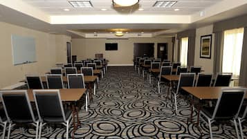 Un salón de conferencias con alfombra estampada, varias mesas y sillas dispuestas para reuniones.