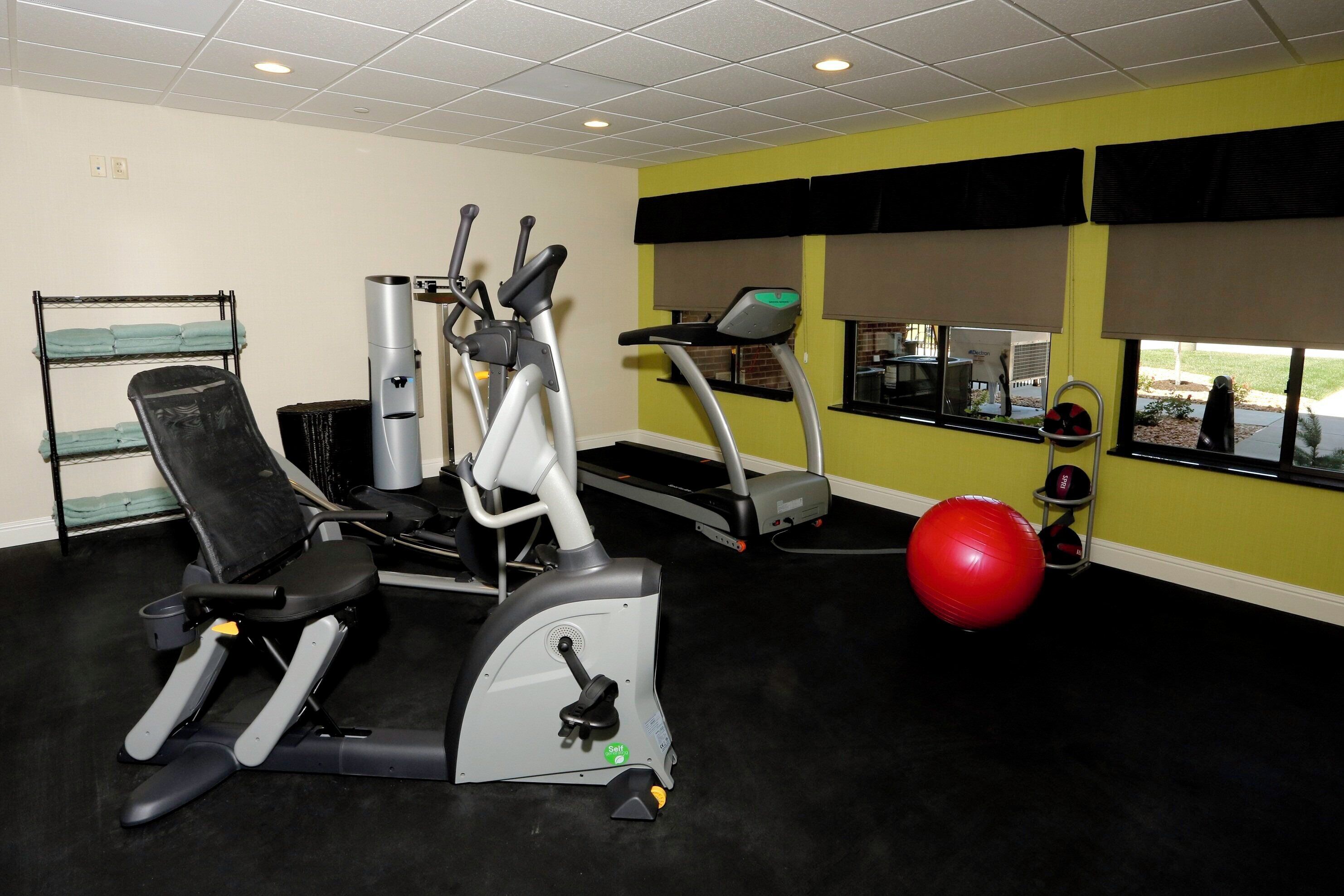Une salle de sport équipée de divers appareils, notamment un vélo d’appartement, un vélo elliptique, un tapis de course et un ballon rouge pour faire de l’exercice.
