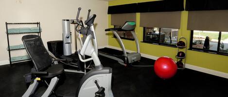 Ein Fitnessraum mit unterschiedlichen Trainingsgeräten, darunter ein Ergometer, ein Crosstrainer, ein Laufband und ein roter Trainingsball.