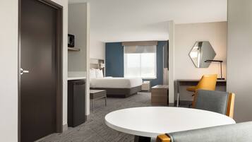 Une chambre d’hôtel avec un lit, un bureau, une chaise, une table ronde et une porte.