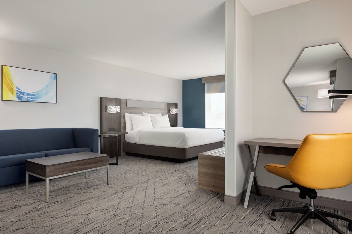 A hotel room with a bed, a desk, a chair, a sofa, and a large mirror.