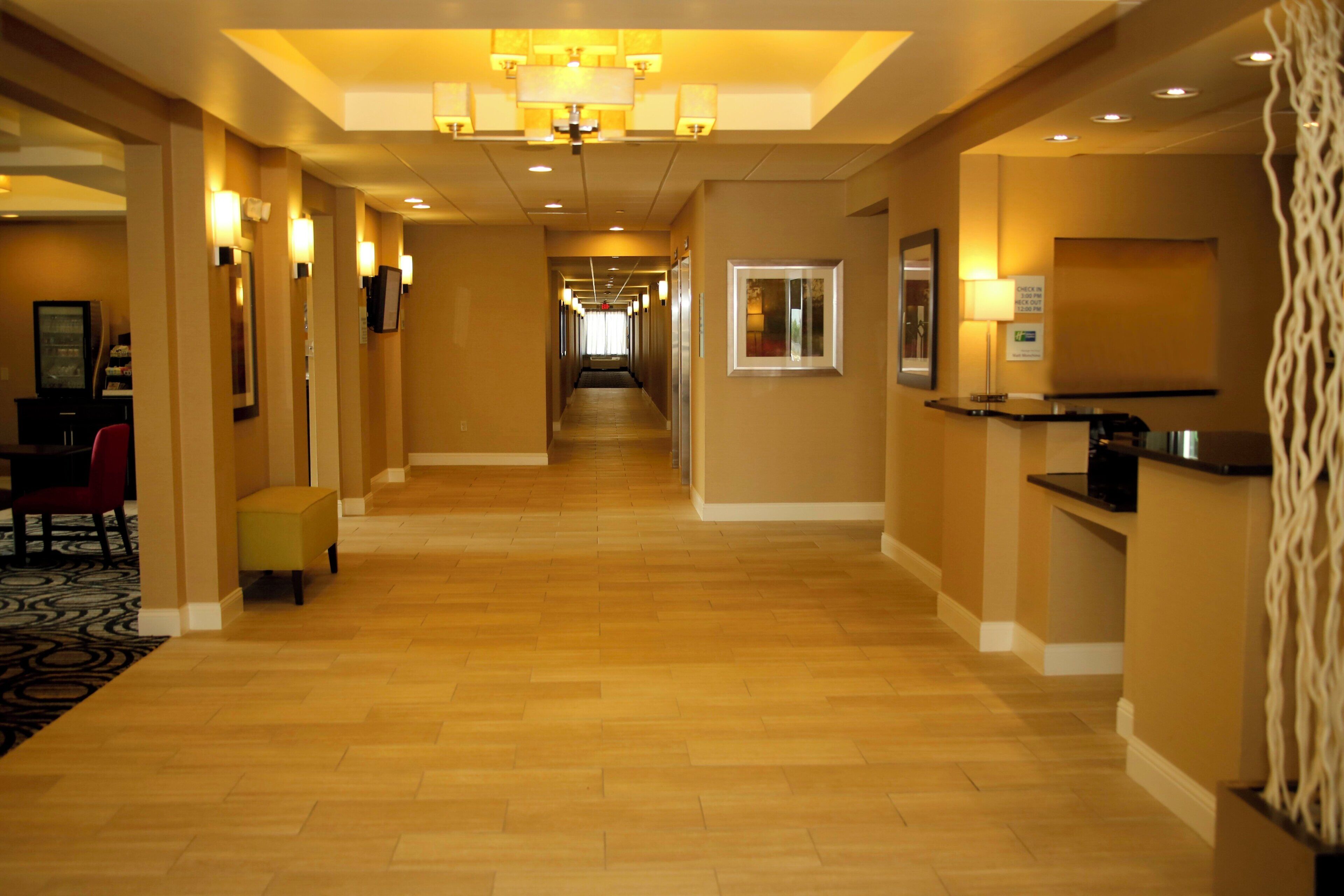A hotel hallway with a reception desk, a check-in counter, and a seating area with a red chair and ottoman.