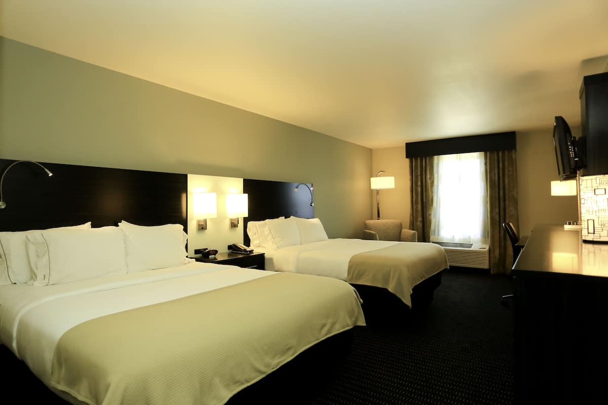 A hotel room with two beds, a desk, a chair, a TV, and a window with curtains.