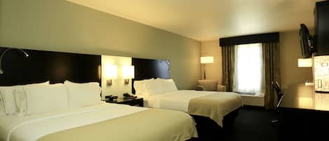 Ein Hotelzimmer mit zwei Betten, einem Schreibtisch, einem Sessel, einem Fernseher und einem Fenster mit Vorhängen.
