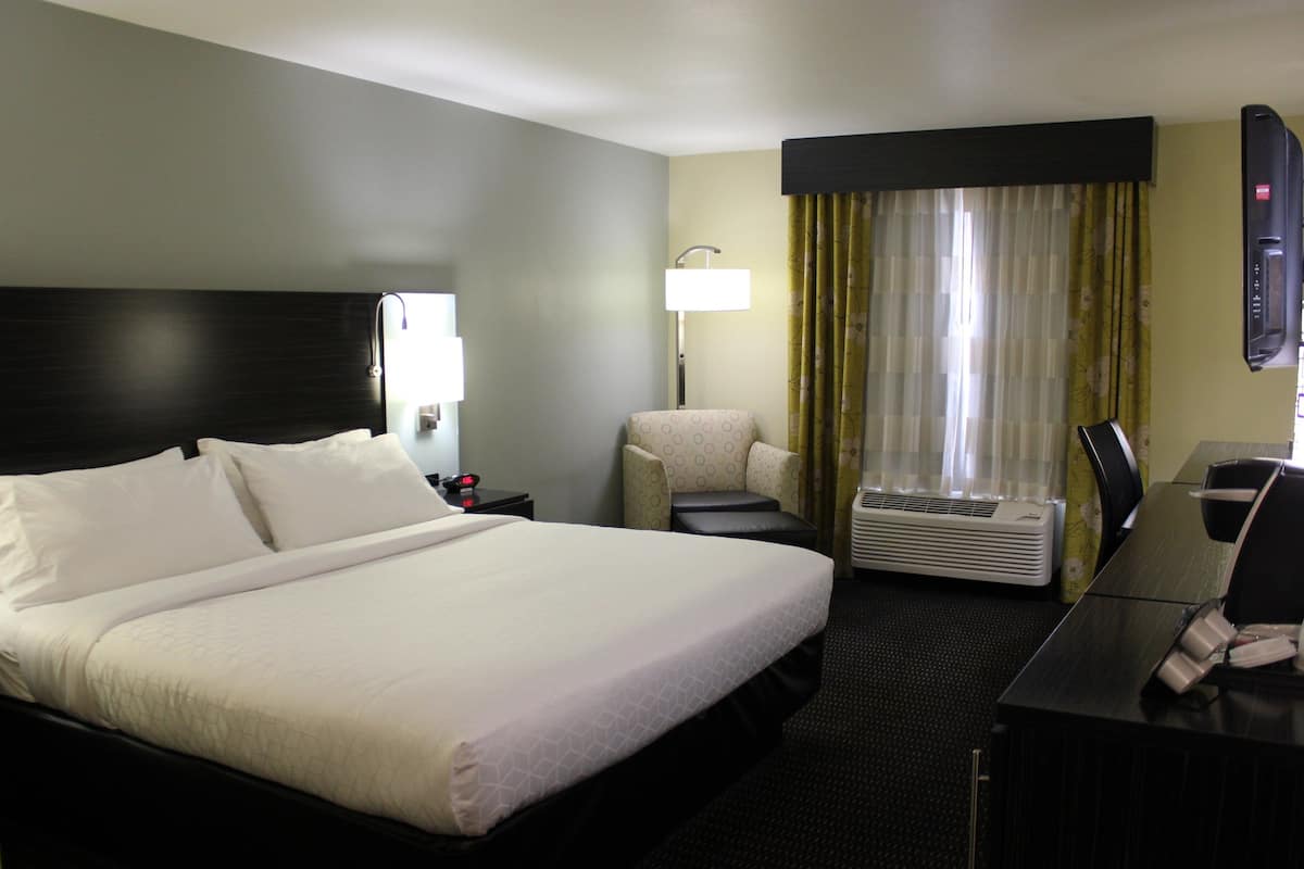 A hotel room with a large bed, a desk with a chair, a lamp, and a window with curtains.