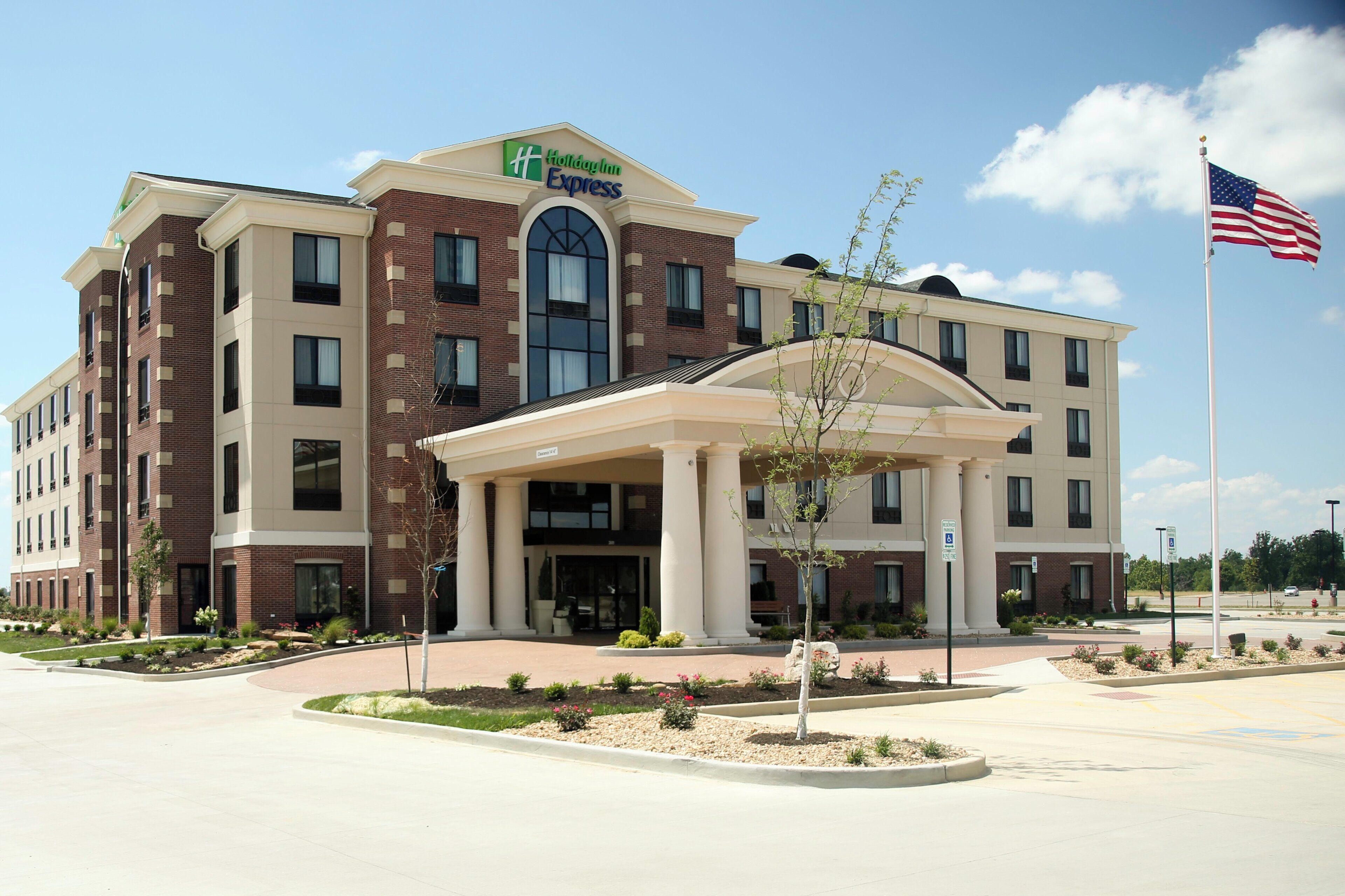 A Holiday Inn Express hotel with a brick facade, a central entrance with a covered walkway, and an American flag.