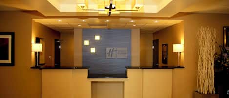 A hotel reception area with a modern chandelier, a reception desk, and a wall-mounted sign for Holiday Inn Express.