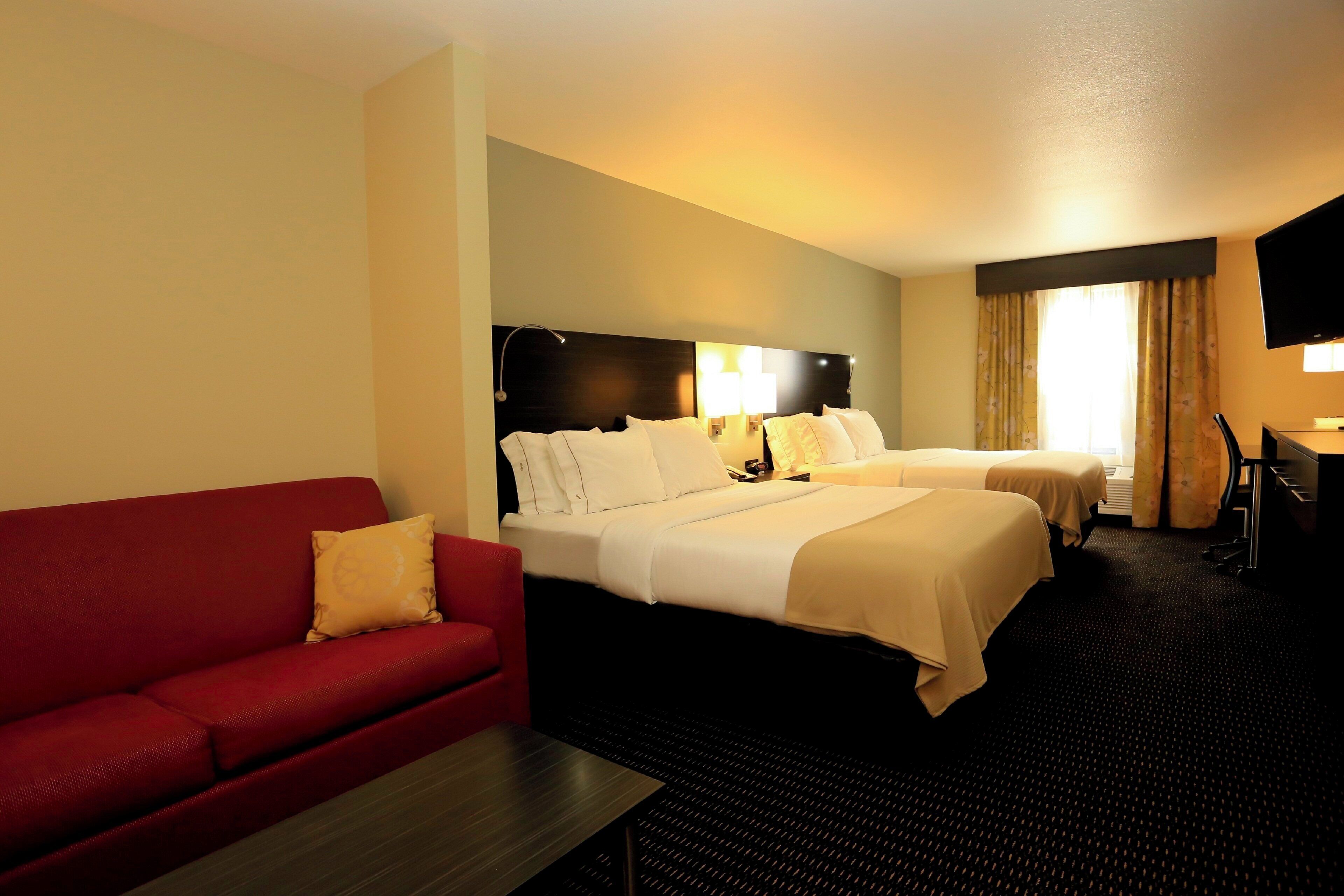 A hotel room with two beds, a red sofa, a desk, and a TV.