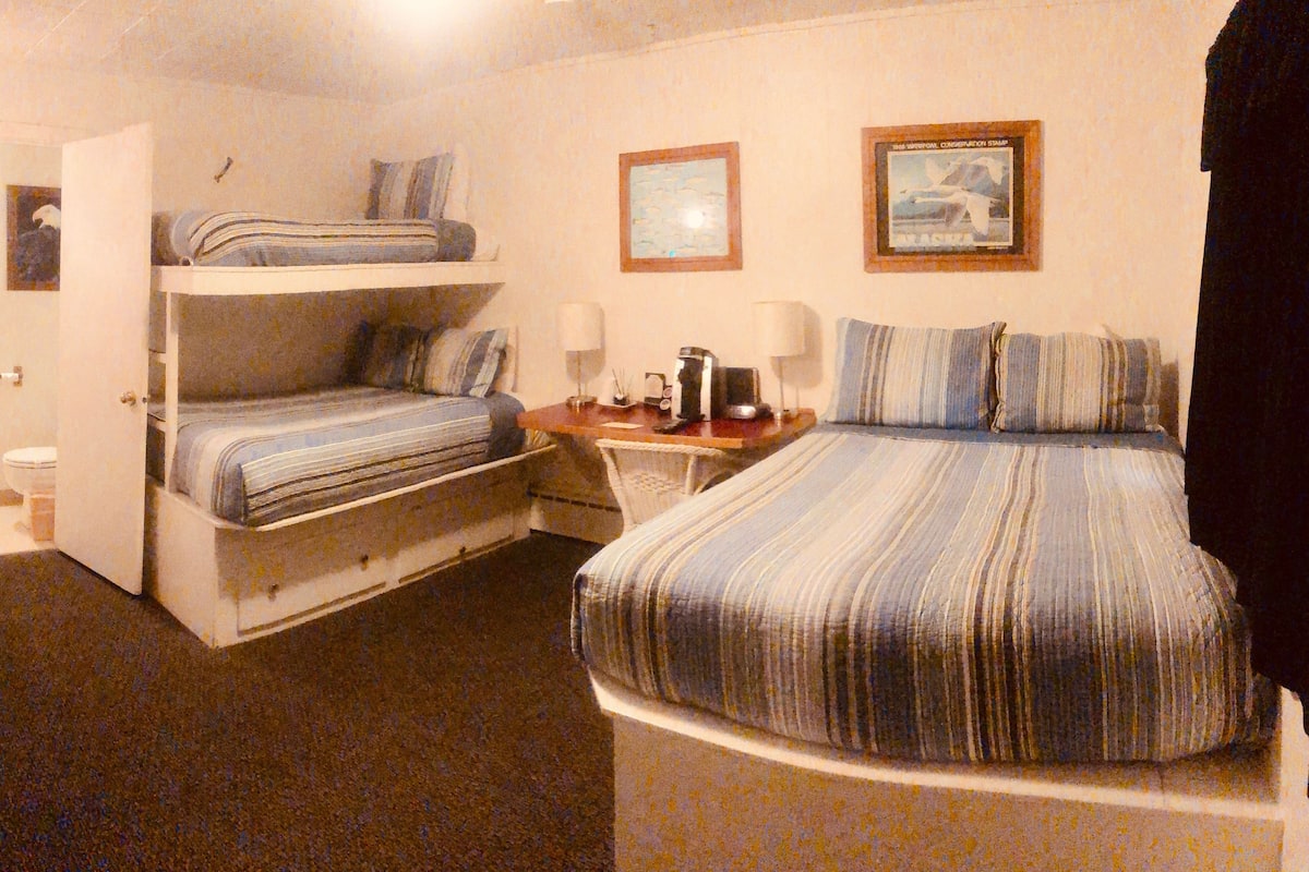 Une chambre d’hôtel compacte comprenant un lit superposé, un bureau avec une chaise, une petite table et un lit simple.