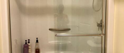 A glass-enclosed shower stall with a glass door, a white toilet, and a shelf with toiletries.