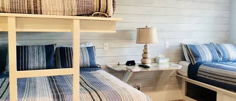A bunk bed with striped bedding, a bedside table with a lamp, and a small nightstand with a clock.