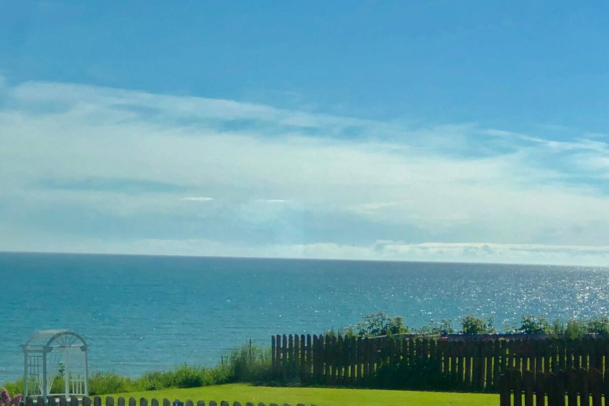 Une vue sur la côte, avec une clôture en bois, une serre en verre et un ciel dégagé.