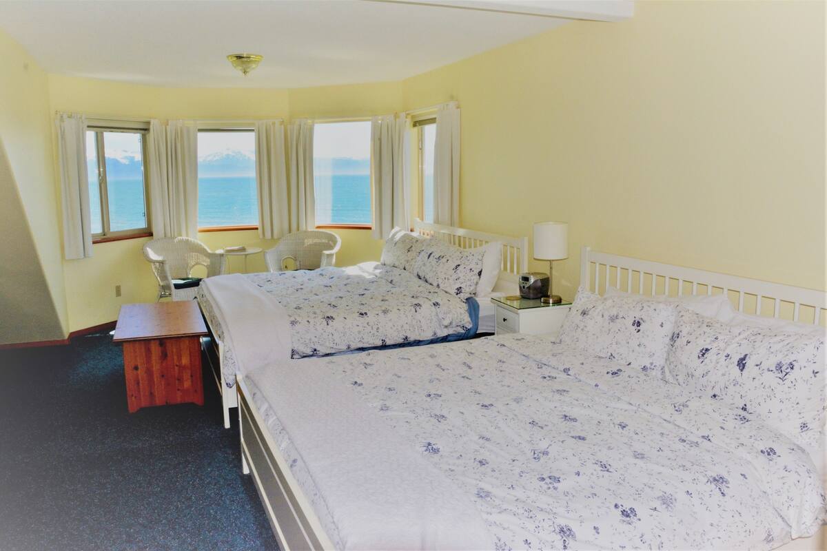 Une chambre d’hôtel avec deux lits, une chaise, une petite table et une vue sur la mer.