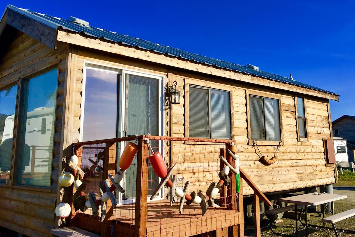 Une cabane en bois avec un toit en métal, de grandes fenêtres et une terrasse dotée de mangeoires à oiseaux.
