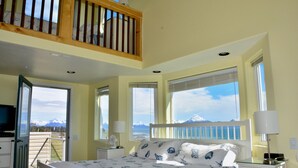 A bedroom with a bed, bedside tables, a TV, and a balcony with a view of mountains. - Driftwood Inn and Seaside Lodges (Homer)
