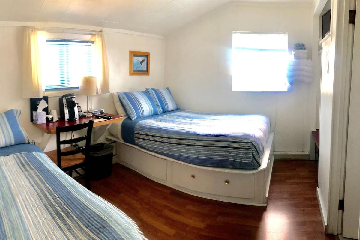 Une petite pièce, de taille modeste, comprenant deux lits simples, un bureau avec une chaise, une fenêtre et une porte.