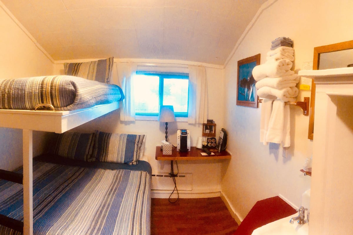 Une petite pièce, de taille modeste, comprenant un lit superposé, un bureau avec un ordinateur, une fenêtre et une salle de bain.