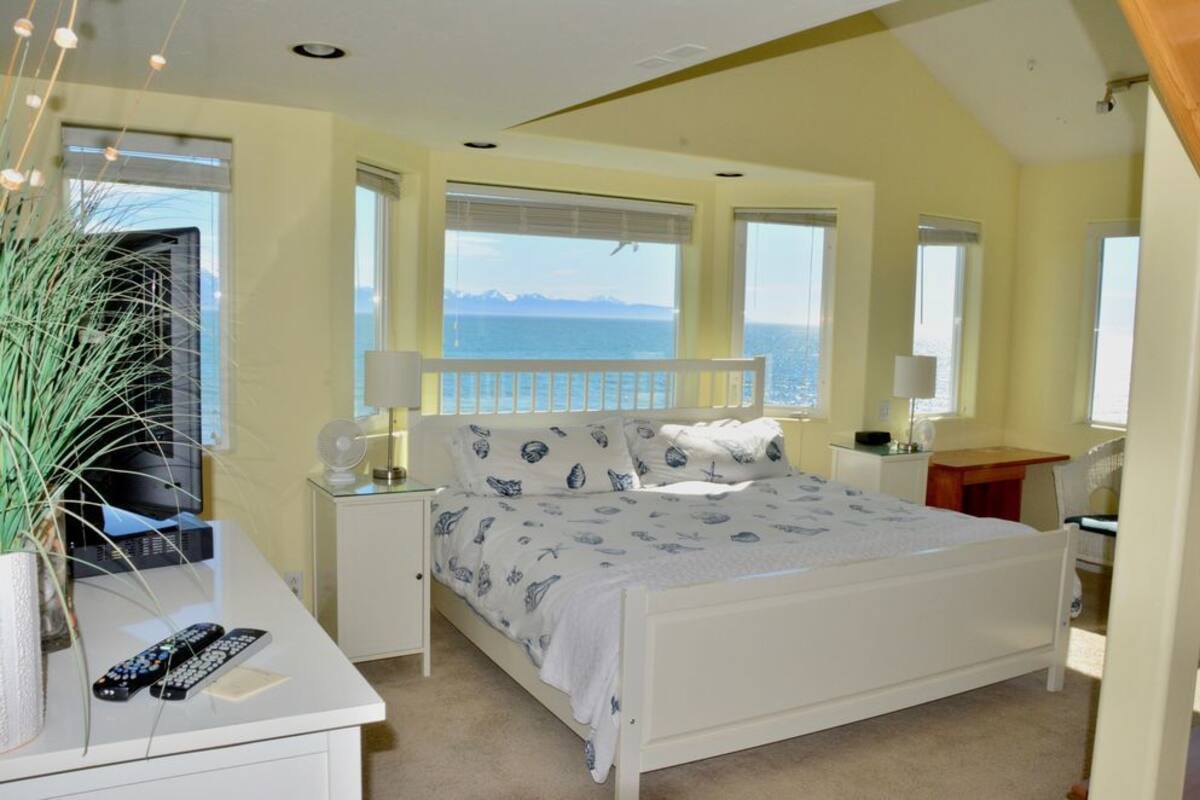 Une chambre à coucher avec un lit, des tables de chevet, un bureau et une vue sur la mer.