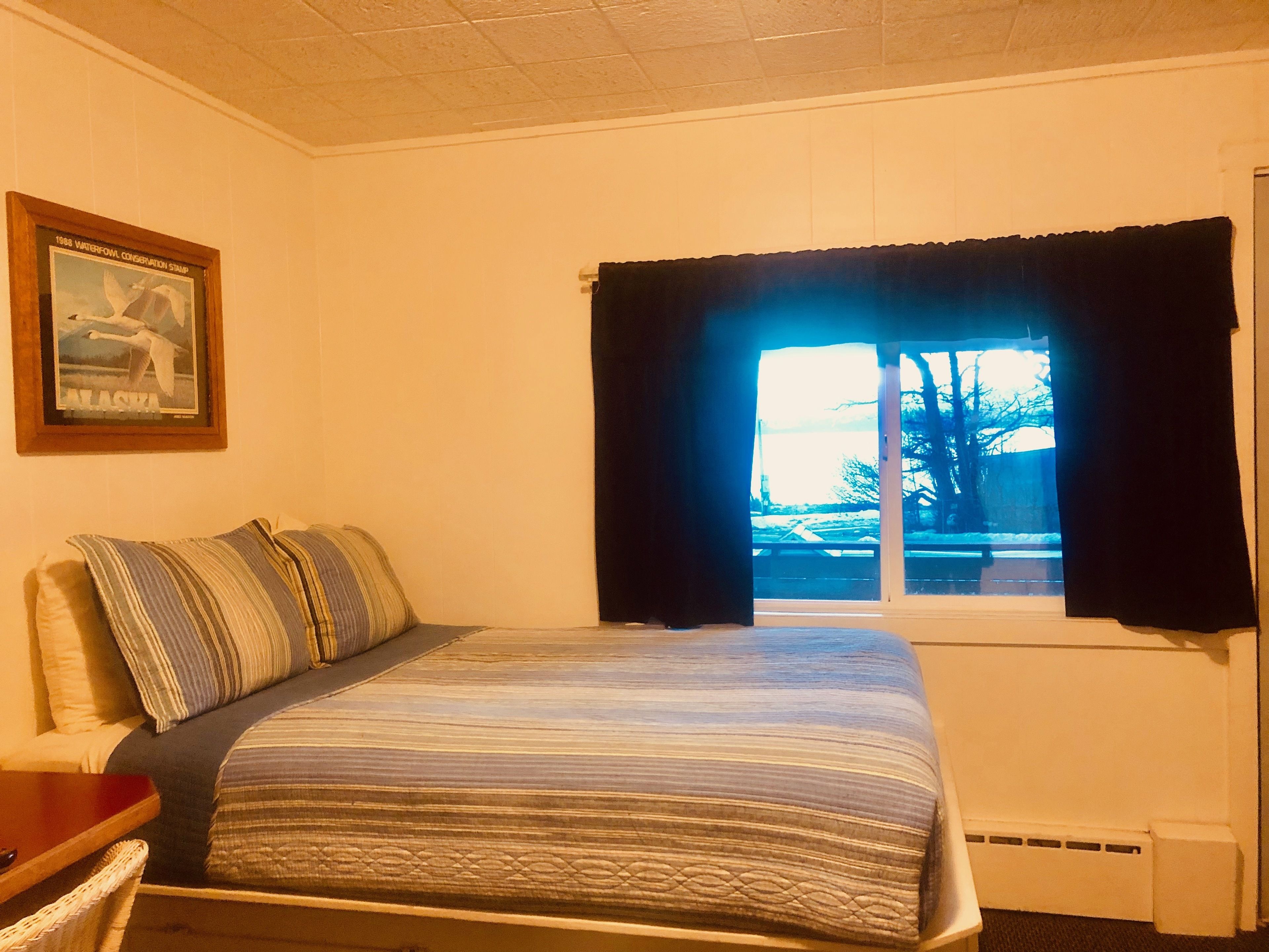 Un dormitorio con cama, ventana con cortinas, un cuadro en la pared y un radiador.