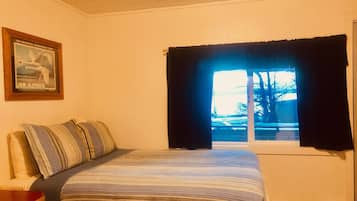 Un dormitorio con cama, ventana con cortinas, un cuadro en la pared y un radiador.