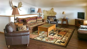 A living room with a sofa, armchairs, a coffee table, and a rug with animal prints. - Driftwood Inn and Seaside Lodges (Homer)