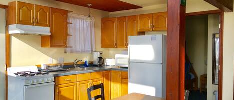 A compact kitchen with wooden cabinets, a stove, a sink, and a refrigerator.
