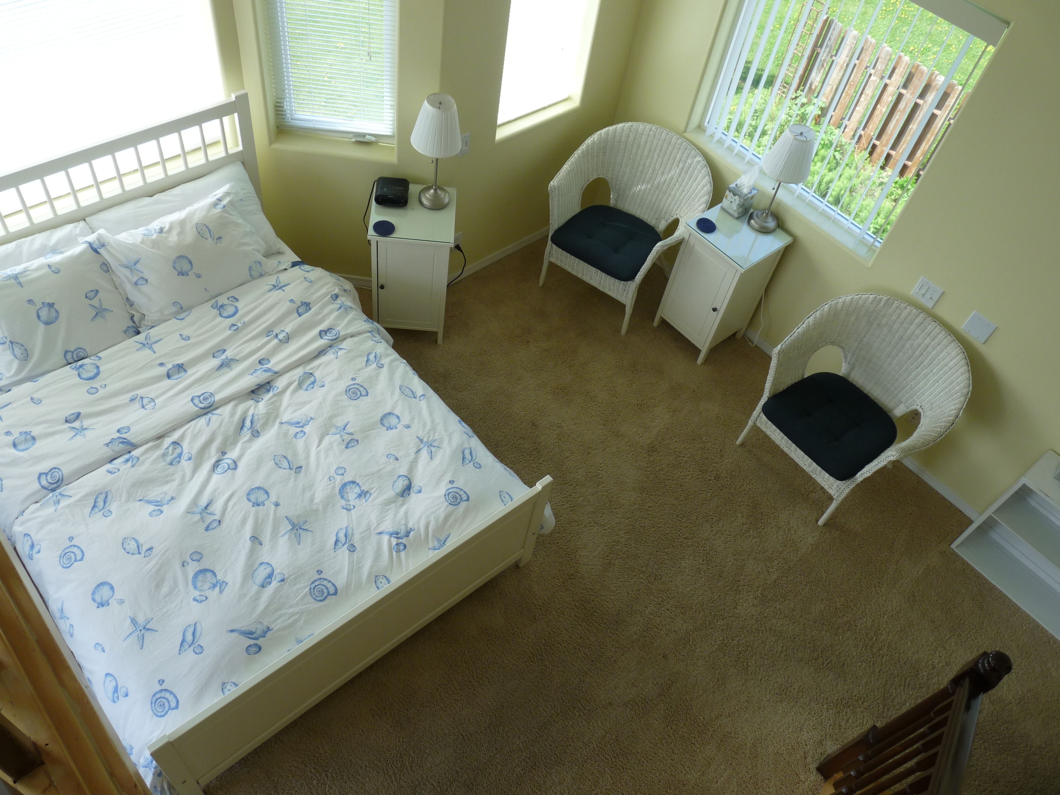 A bedroom with a bed, two nightstands, two chairs, a window, and a door.