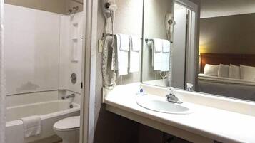 A bathroom with a bathtub, toilet, and a large mirror above the sink.