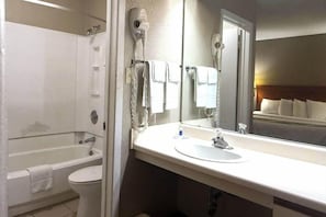 A bathroom with a bathtub, toilet, and a large mirror above the sink.