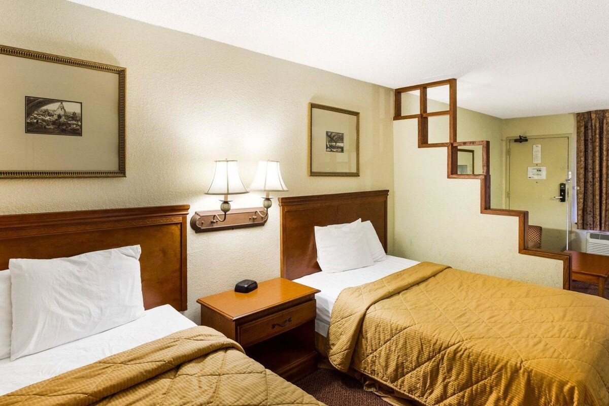 A hotel room with two beds, a nightstand, a lamp, a framed picture, and a mirror.