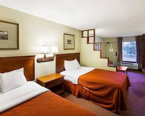 A hotel room with two beds, a nightstand, a lamp, a framed picture, and a staircase leading to a balcony.