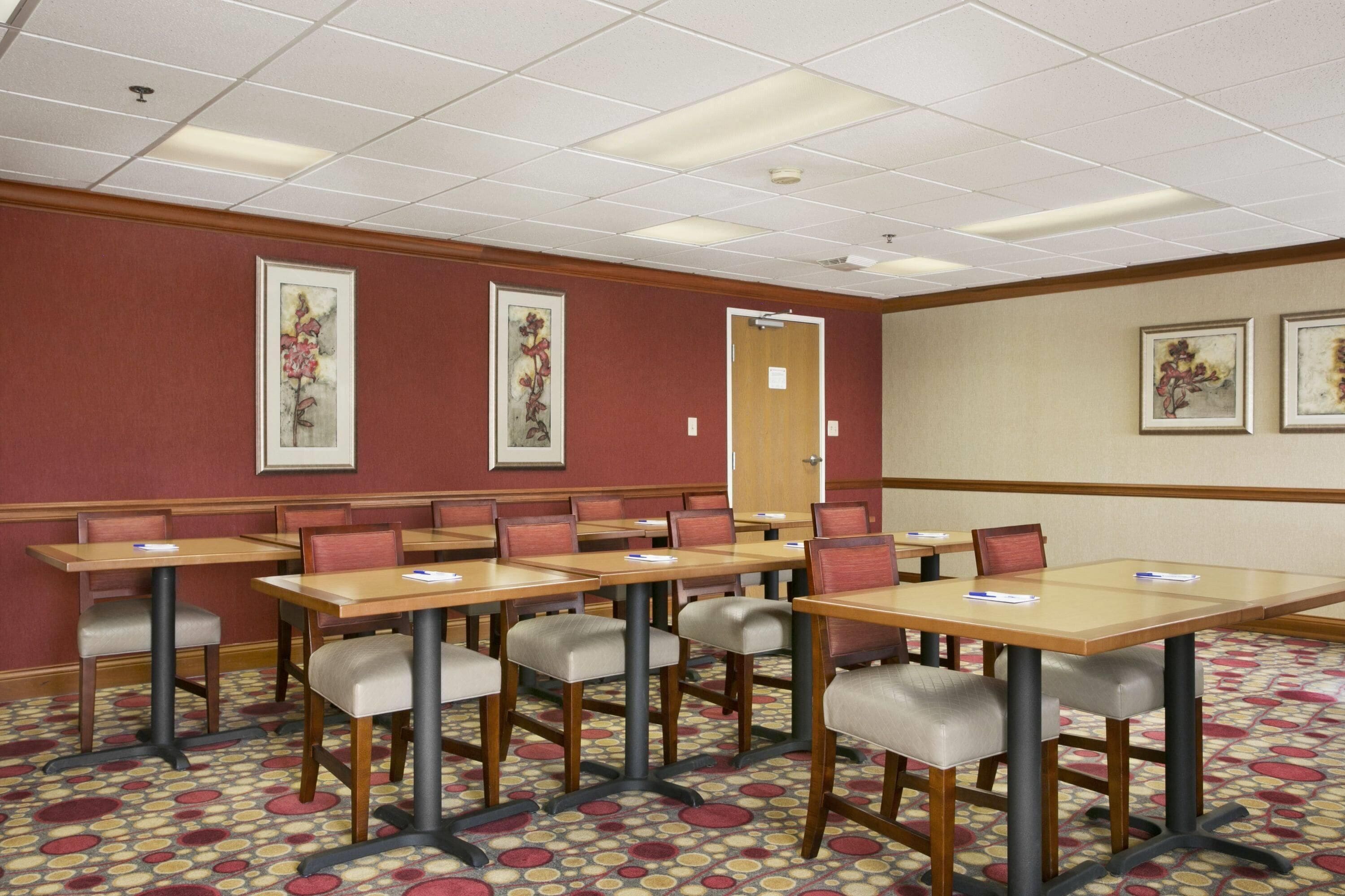A conference room with multiple tables and chairs, a patterned carpet, and framed artwork on the walls.