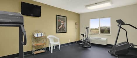 A gym with exercise equipment, a television, a window, and a chair.