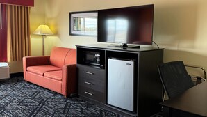 A hotel room with a sofa, a small refrigerator, a microwave, a flat-screen TV, a lamp, and a window with curtains. - Baymont by Wyndham Evansville North/Haubstadt (Haubstadt)