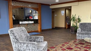 A reception area with a counter, chairs, a patterned carpet, and a potted plant. - Baymont by Wyndham Evansville North/Haubstadt (Haubstadt)