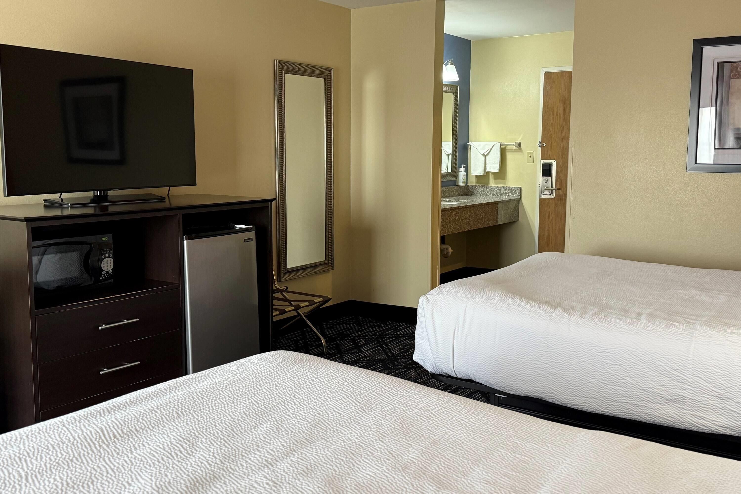 A hotel room with two beds, a TV, a minibar, and a bathroom visible through an open door.